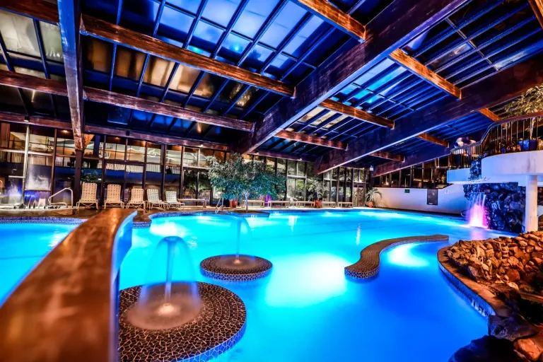Indoor pool with many lights underwater, fountains, in large space.